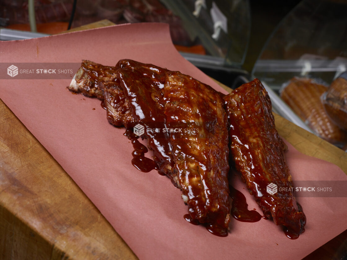 3 full racks of barbecued ribs covered in BBQ sauce on butcher's paper on a butcher's block