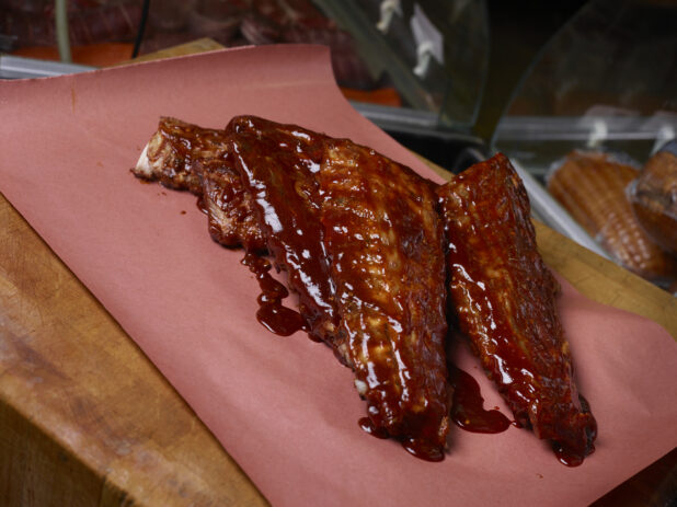 3 full racks of barbecued ribs covered in BBQ sauce on butcher's paper on a butcher's block
