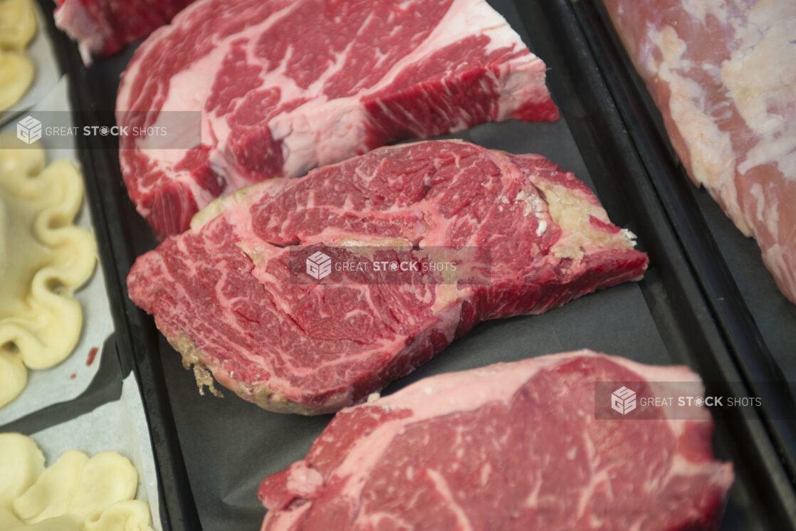 Fresh cut steaks in a display case on a black background, close-up, overhead view