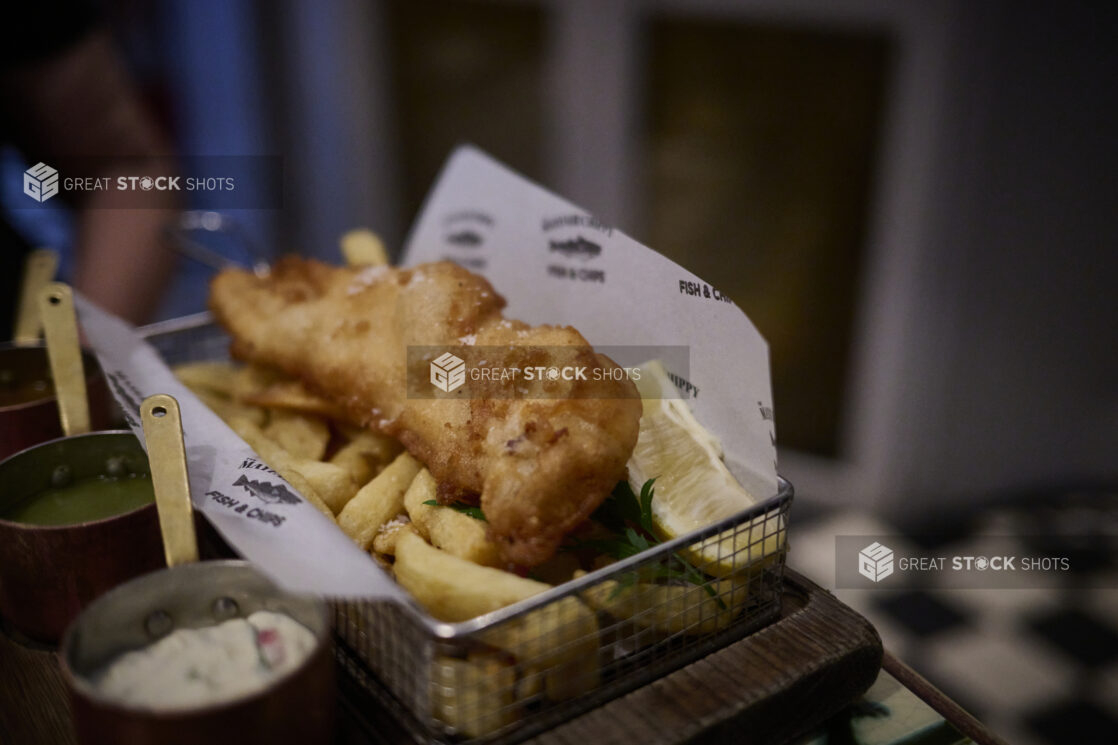 Fish and chips in a personal size wire basket with dipping sauces in mini copper pots on the side]