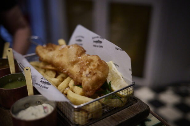 Fish and chips in a personal size wire basket with dipping sauces in mini copper pots on the side]