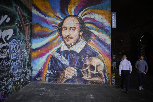 Mural of William Shakespeare holding a skull and a quill on a wall in London, England with people walking by the mural