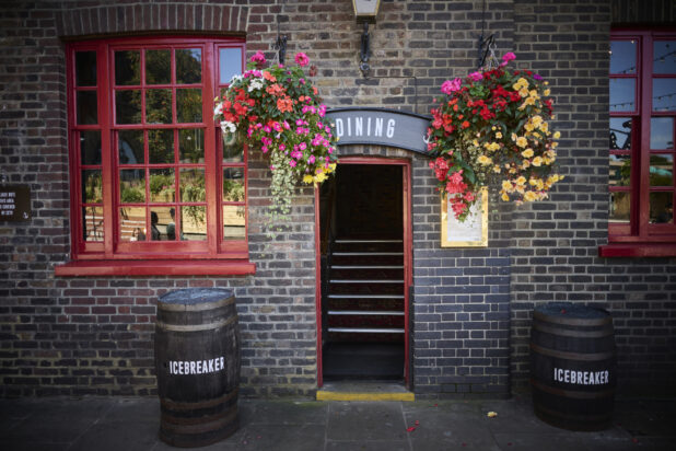 Restaurant facade with red windows, hanging flowers, wooden barrels and sign above the door saying "Dining"