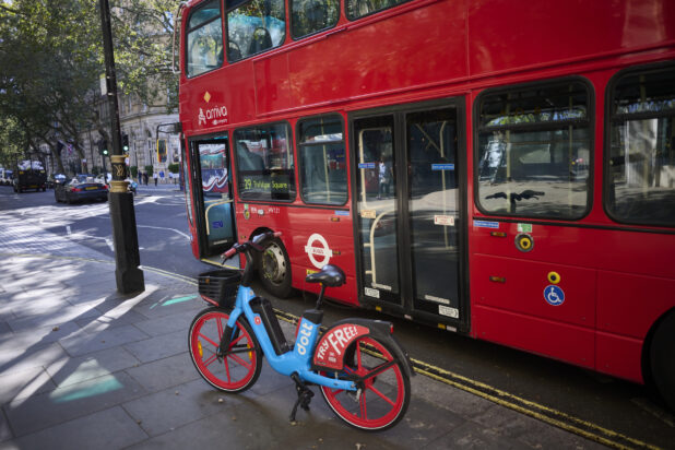 Double decker bus at a bus stop with a vibrant coloured e-bike next to it on a London, England road