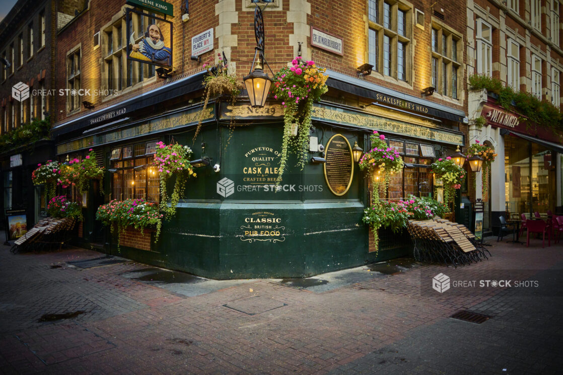 A oldstyle pub on a street corner with a lantern overhead, flowers and folded tables and chairs in London, England,