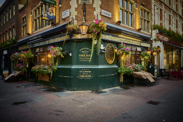 A oldstyle pub on a street corner with a lantern overhead, flowers and folded tables and chairs in London, England,
