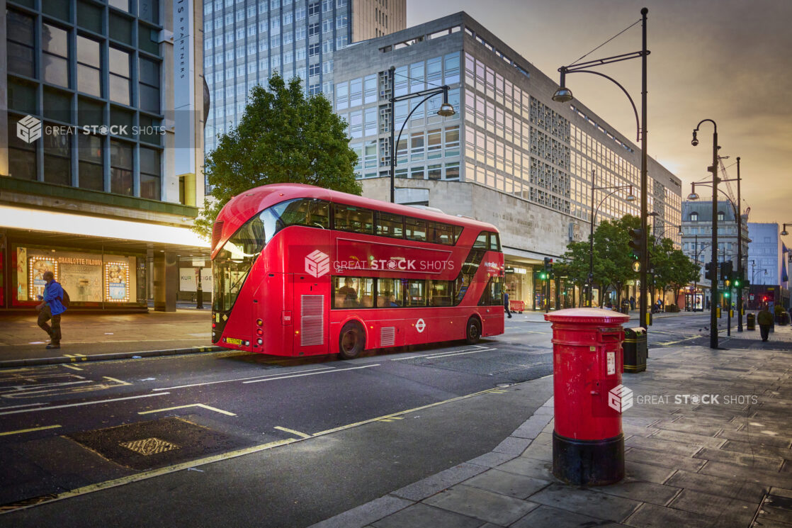 View of a London street with a red double decker bus and a red mailbox, postbox