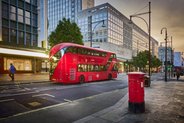 View of a London street with a red double decker bus and a red mailbox, postbox