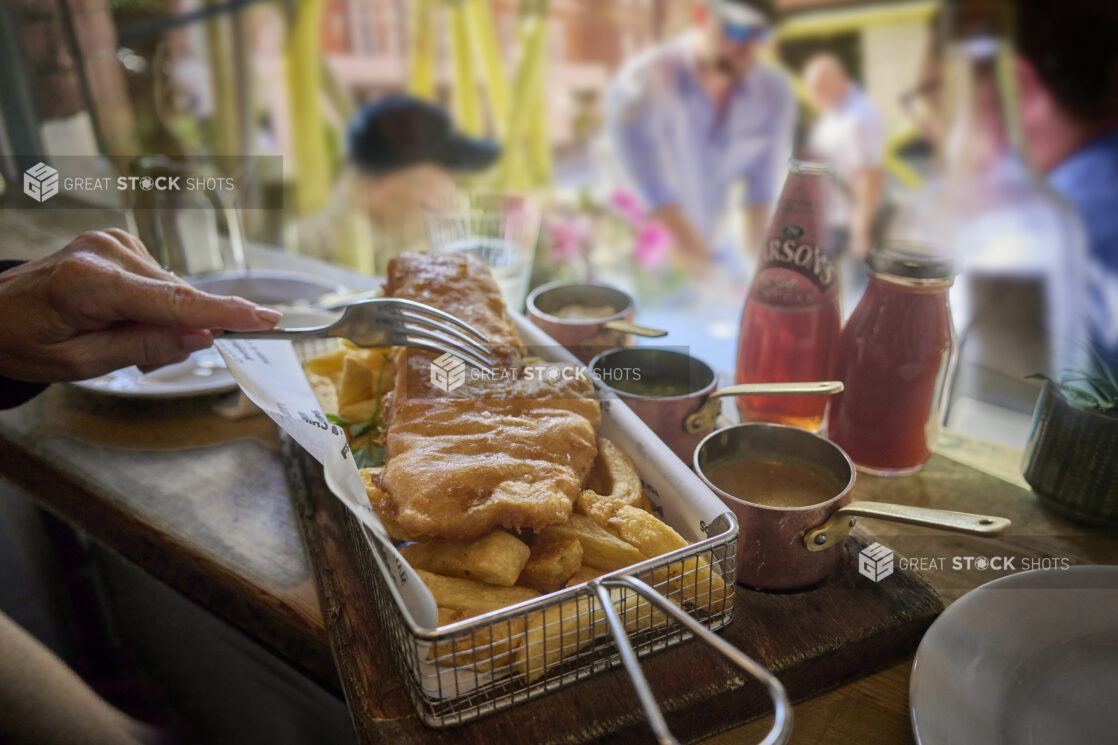 Close up of a Basket of Classic British Fish and Chips with tins of gravy and sauces