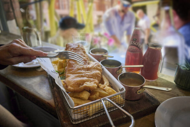 Close up of a Basket of Classic British Fish and Chips with tins of gravy and sauces