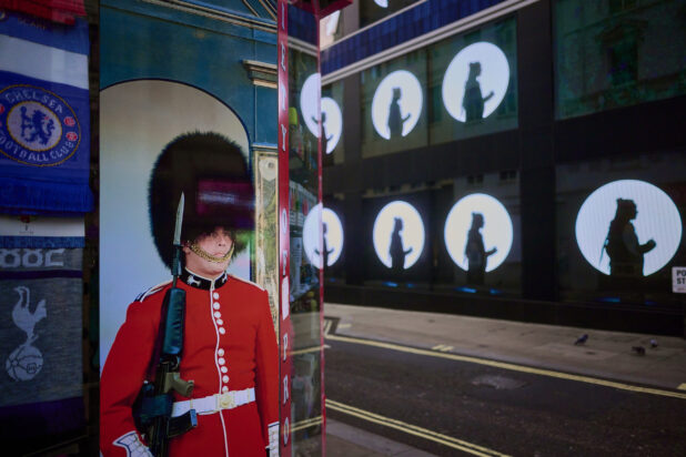Picture of a "Queens's Guard" on a storefront on the corner of a street with an LED video wall across the street