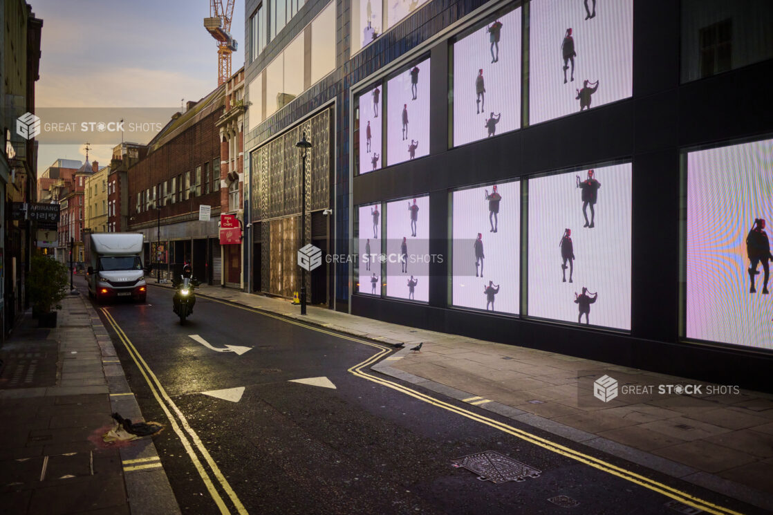 View of a street with video screens on the side of a building, person on a motorbike, delivery truck, one way street, London, England