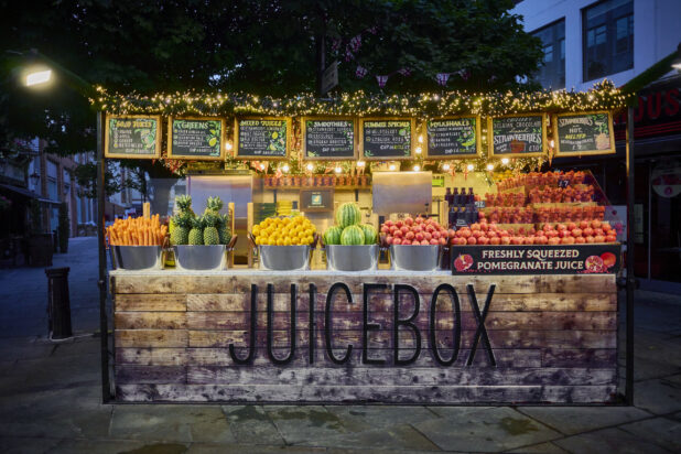 Straight on view of an outdoor juice stand with fresh fruits and vegetables, vibrant colours,