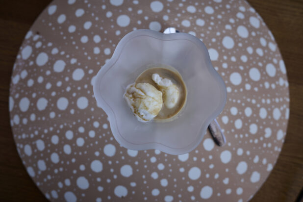 Affogato, hot coffee with ice cream in a frosted parfait glass on a coffee colored plated with white dots