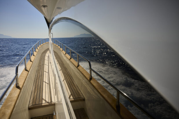 Symmetrical Medium shot of the side walkway of a Yacht with the Mediterranean Sea in the background, and the sea and walkway reflected in the windows