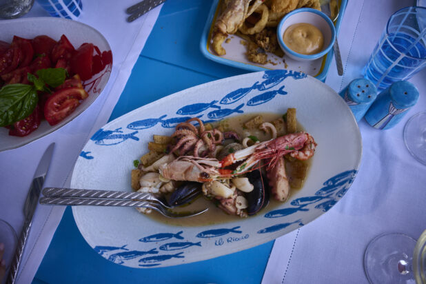 Overhead view of a Mediterranean style meal with a fresh seafood platter, fried seafood platter, fresh tomatoes and basil with seafood patterned dishes, bright blue accessories