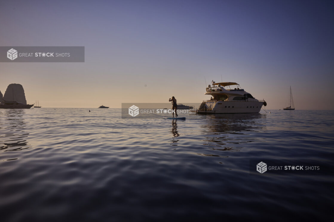 Wide Shot of Ocean, Paddle Boarder and Yacht in Background at Sunset