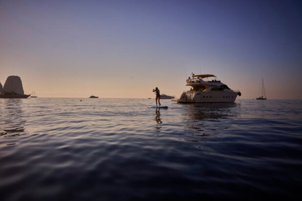 Wide Shot of Ocean, Paddle Boarder and Yacht in Background at Sunset