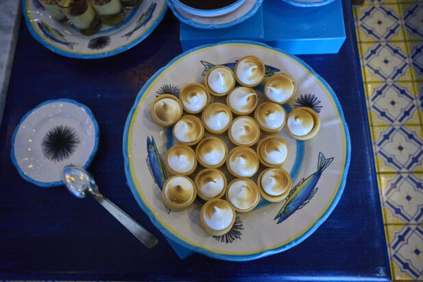 Overhead view of a platter of mini lemon meringue tarts on a table with bright blue accents and Italian tiles