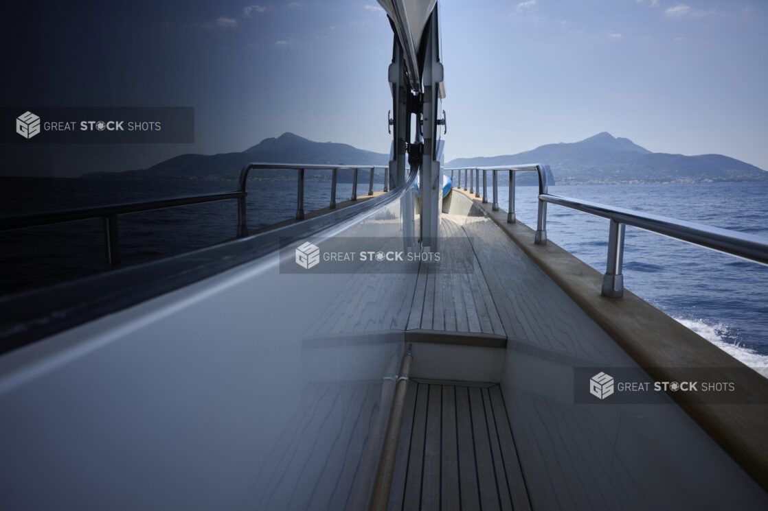 Symmetrical Medium Shot of the Side Walkway of a Yacht with the Ocean, Coastline and Mountains Reflected in the Window