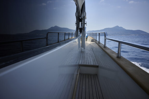 Symmetrical Medium Shot of the Side Walkway of a Yacht with the Ocean, Coastline and Mountains Reflected in the Window