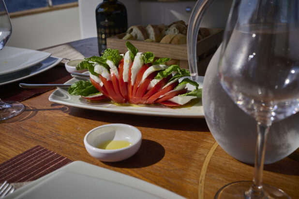 Caprese Salad on a Wooden Table with Olive Oil, Bread in background and a pitcher of water and a wine glass