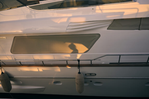Close up side view of a yacht at sunset with a shadow silhouette of a person in the sunset against the side of the yacht