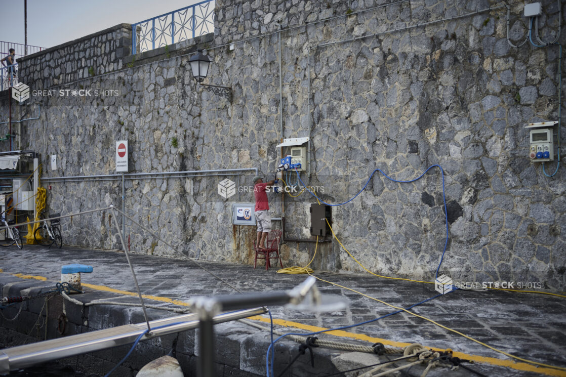 Man standing on a red wicker chair against a stone wall on a walkway at the seaside on the Amalfi coast in Italy