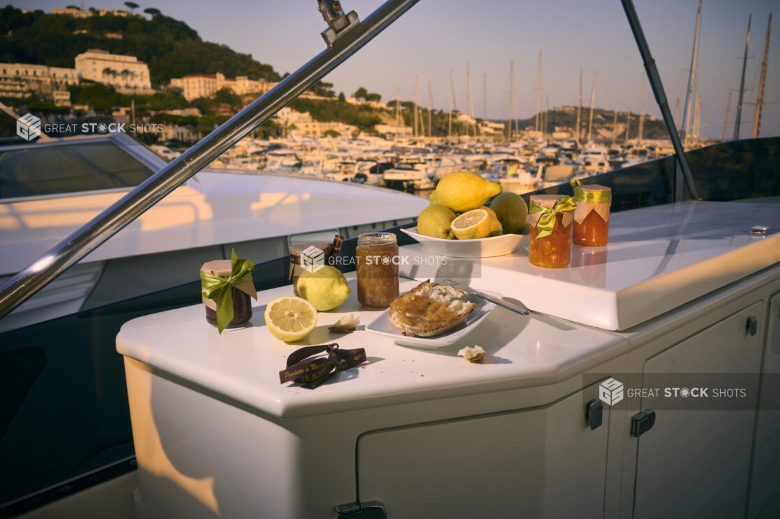 Snack of crusty bread, preserves and fresh lemons on a yacht with a marina and hillside in Italy in the background