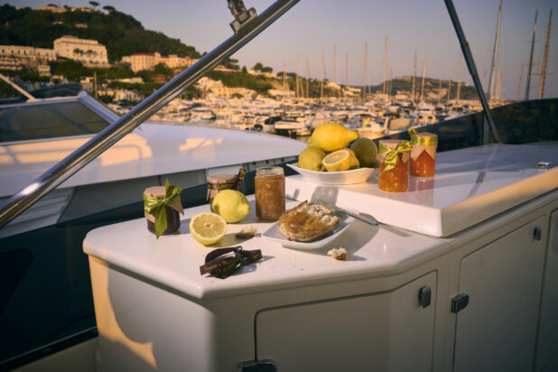 Snack of crusty bread, preserves and fresh lemons on a yacht with a marina and hillside in Italy in the background