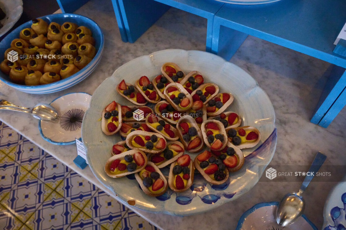 Overhead view of a platters of Italian desserts on a marble table with bright blue accents and Italian tiles