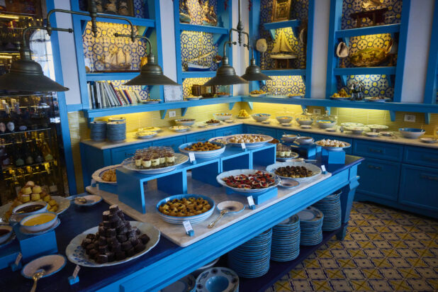 View of an exquisite Mediterranean kitchen with bright blue, yellow and marble dishes and finishes with delectable desserts displayed
