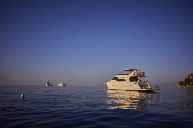 View of a yacht on the water with other yachts, boats and a hillside in the background