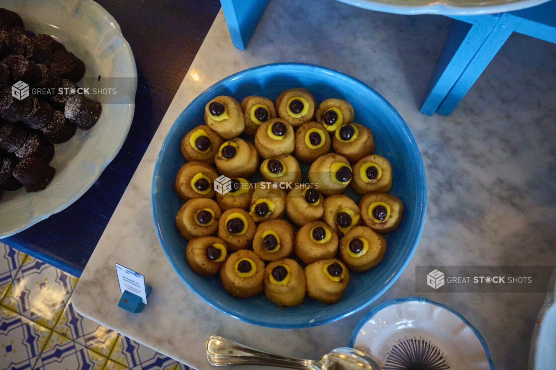 Overhead view of a bright blue bowl of Italian desserts on a marble table with bright blue accents and Italian tiles