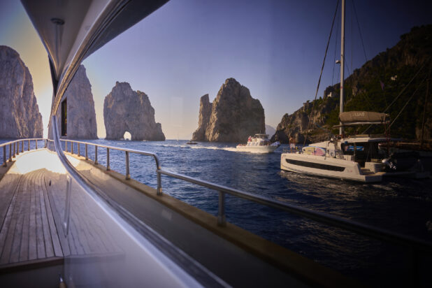 View of the sea with boats, Faraglioni rock formations and mountainside reflected off a window on a yacht, Capri, Italy