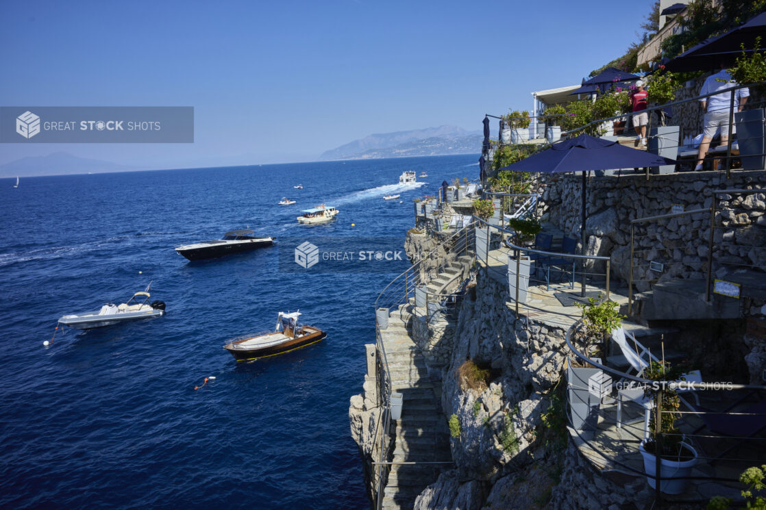 Breathtaking view of a multi-tiered restaurant, yachts, boats and mountains in the distance on the coast of the Mediterranean sea