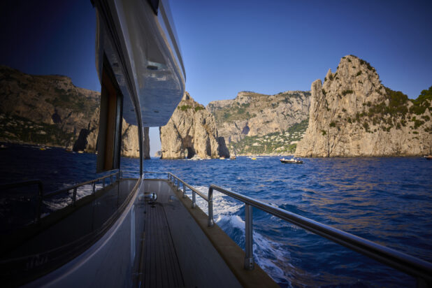 Medium Shot of the Side Walkway of a Yacht with the Ocean, Italian Coast and Mountains Reflected in the Window