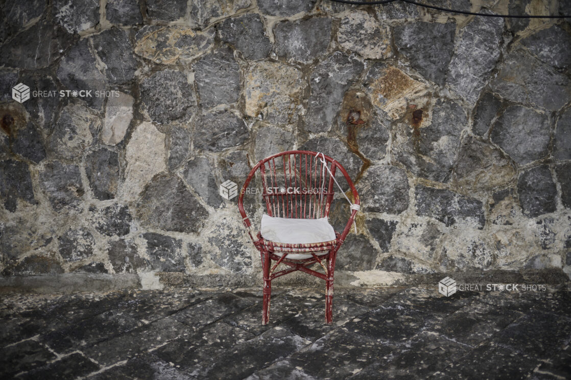 Weathered red wicker chair against a stone wall