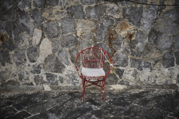 Weathered red wicker chair against a stone wall