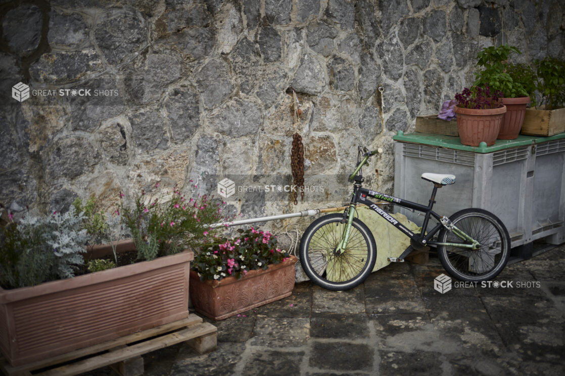 Flowers in planters and pots with a bicycle against a stone wall