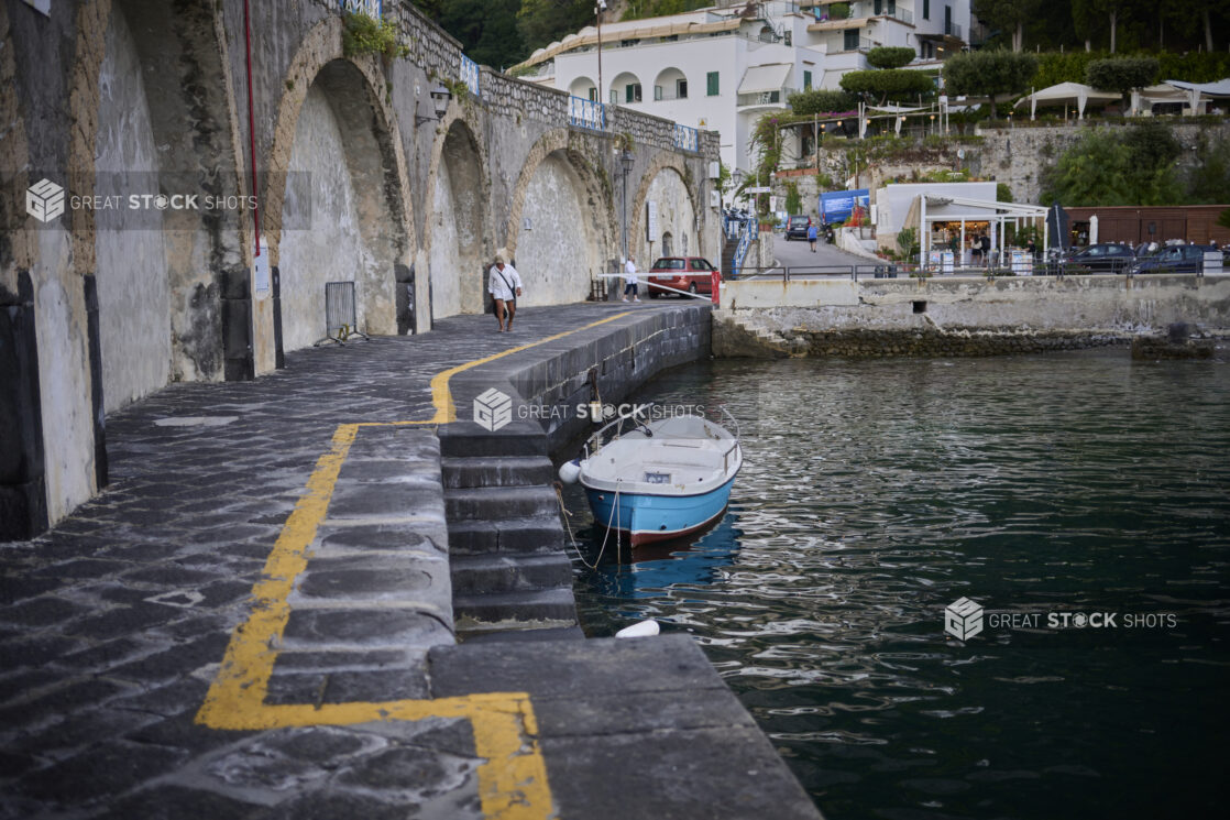 Waterside walkway with stairs down to the water with a small boat in the water on the Amalfi coast, Italy