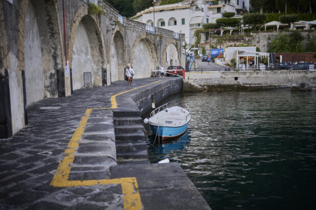 Waterside walkway with stairs down to the water with a small boat in the water on the Amalfi coast, Italy