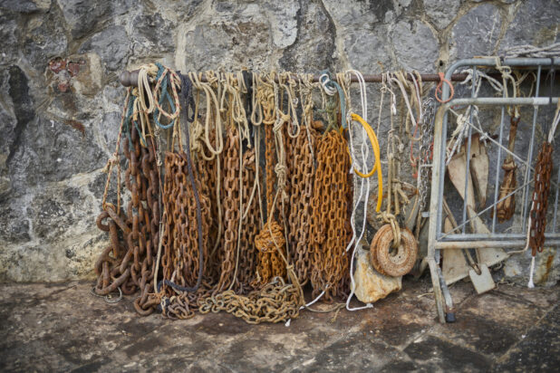Fishing ropes, chains and weights against a stone wall in Italy