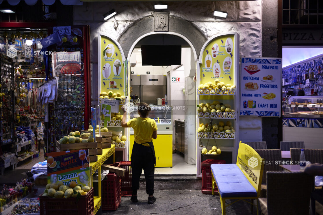 Gelato/refreshment stand in Italy at night, bright colours, with souvenir shop adjacent