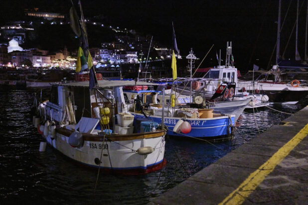 View of a harbour with boats and hillside at night in Italy