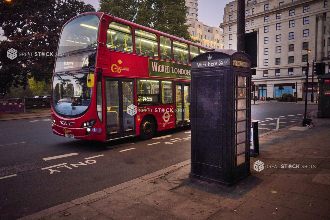 Double decker bus on a street in London, England with a telephone box on the sidewalk