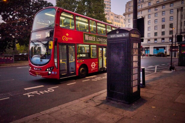 Double decker bus on a street in London, England with a telephone box on the sidewalk