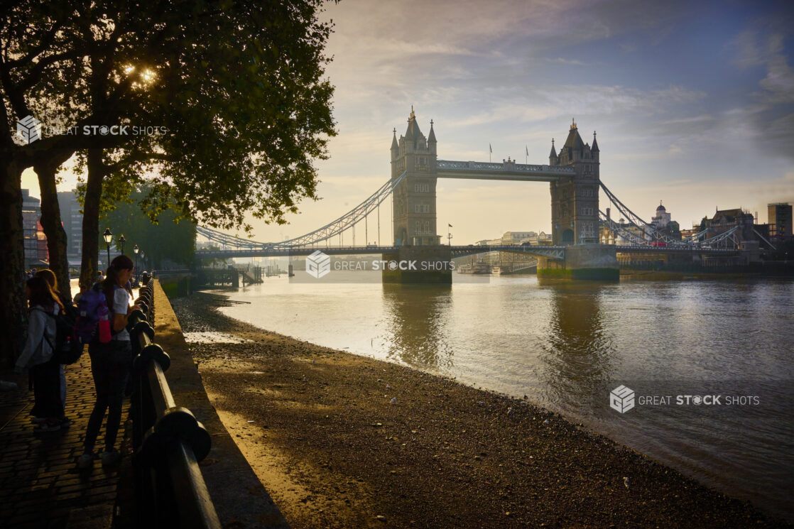 Dawn view of the Tower of London from the Queen's Walk along the Thames River with people standing around