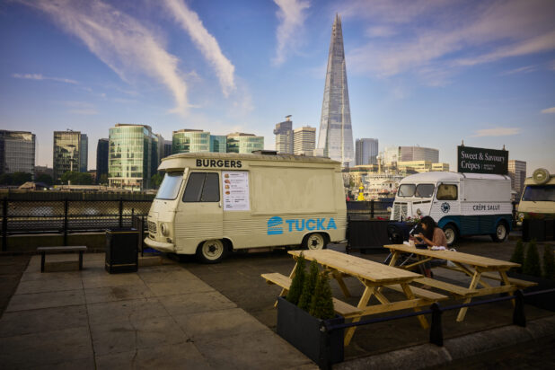 Old style food trucks along the waterfront in London, England with picnic tables and greenery surrounding