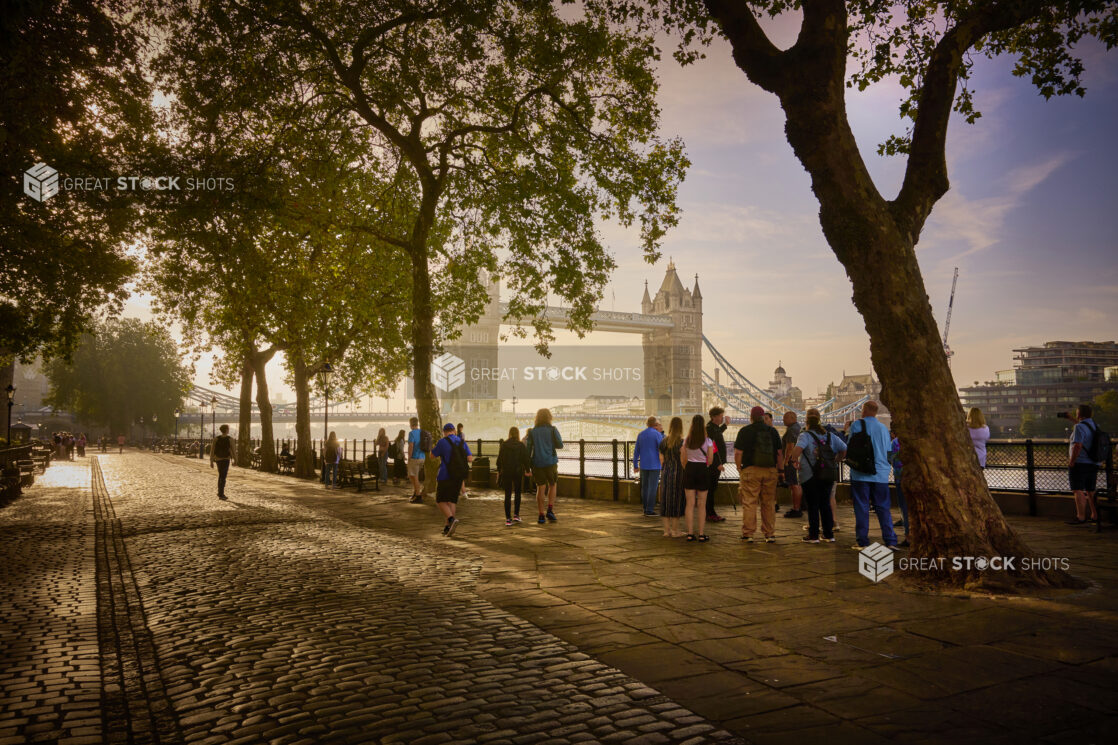 Dawn view of the Tower of London from the Queen's Walk along the Thames River with people standing around